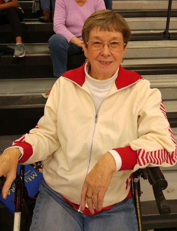 Sue Coller smiles while sitting at a basketball game.