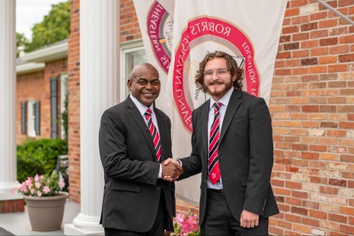 President Dr. Rupert A. Hayles Jr. and Aaron Hitchcock smile and shake hands.