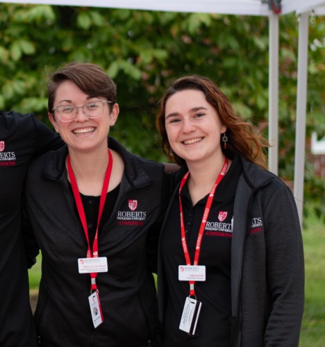 Becca and Addie wear black Roberts jackets and red lanyards and smile.