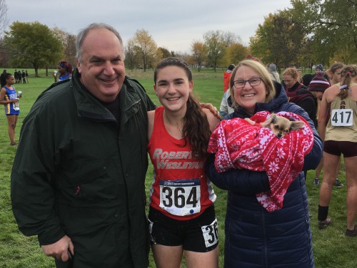 Addie wears a Roberts cross country uniform and smiles with her parents