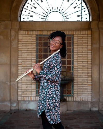 Anaya stands and smiles with her eyes closed while holding a flute against her shoulder.
