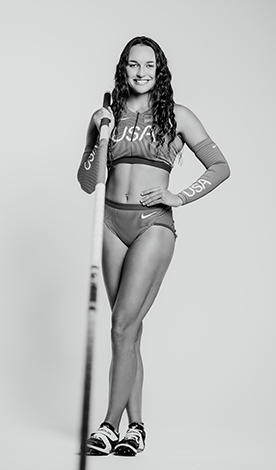 Brynn King smiles while wearing a USA track uniform and holds a pole vault pole