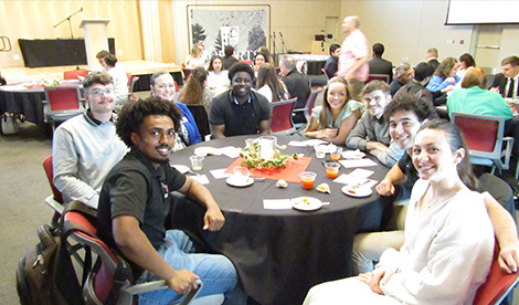 Business students sit at table and smile.