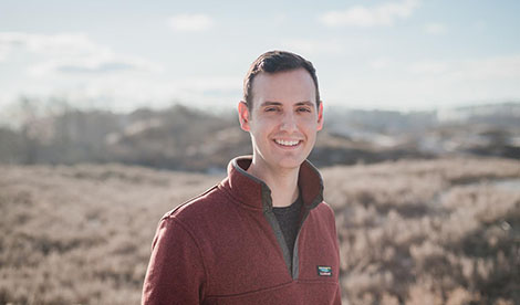 Andrew smiles. The sky and a field are visible behind him. 