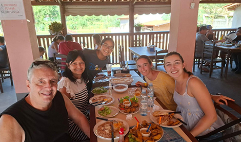 A group sits around a table, smiling, with plates of food in front of them.