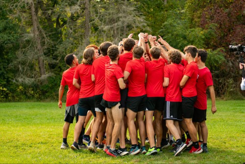 A men's cross country team gathers in a huddle.