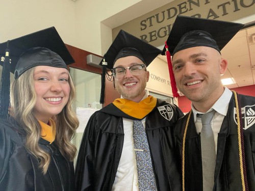 A young women and 2 men smiling in black graduation caps and gowns.