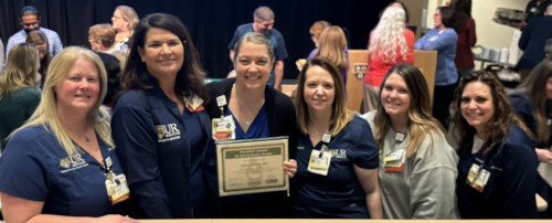 6 women smile. One holds an award certificate.