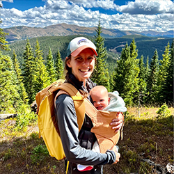 Lauren smiles on a mountain while holding a baby.
