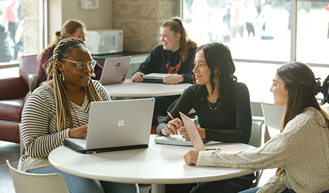 3 students study together. 2 other students are also studying in the background.