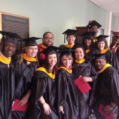 A group of graduates in black caps and gowns with yellow sashes.