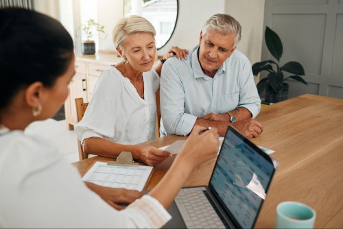 A woman sits in front of a laptop and speaks with an older couple