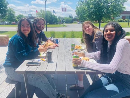 4 students sit at a table outside and smile.