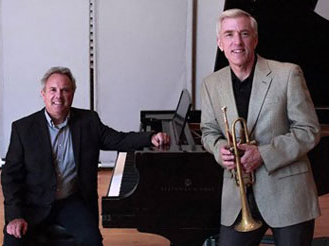 Stephen Shewan smiles at piano while Paul Shewan smiles while standing and holding a trumpet