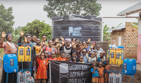 A group of Ugandan's smile and wave with a Ugandan Water Project banner.