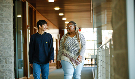 2 students walk and talk to each other in the library.