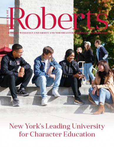 The cover of Voices of Roberts with 4 students sitting on campus and the word Roberts overlayed largely.