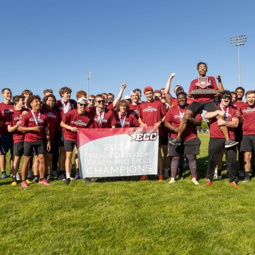 The men's track and field team smiles with their championship  trophy and banner.