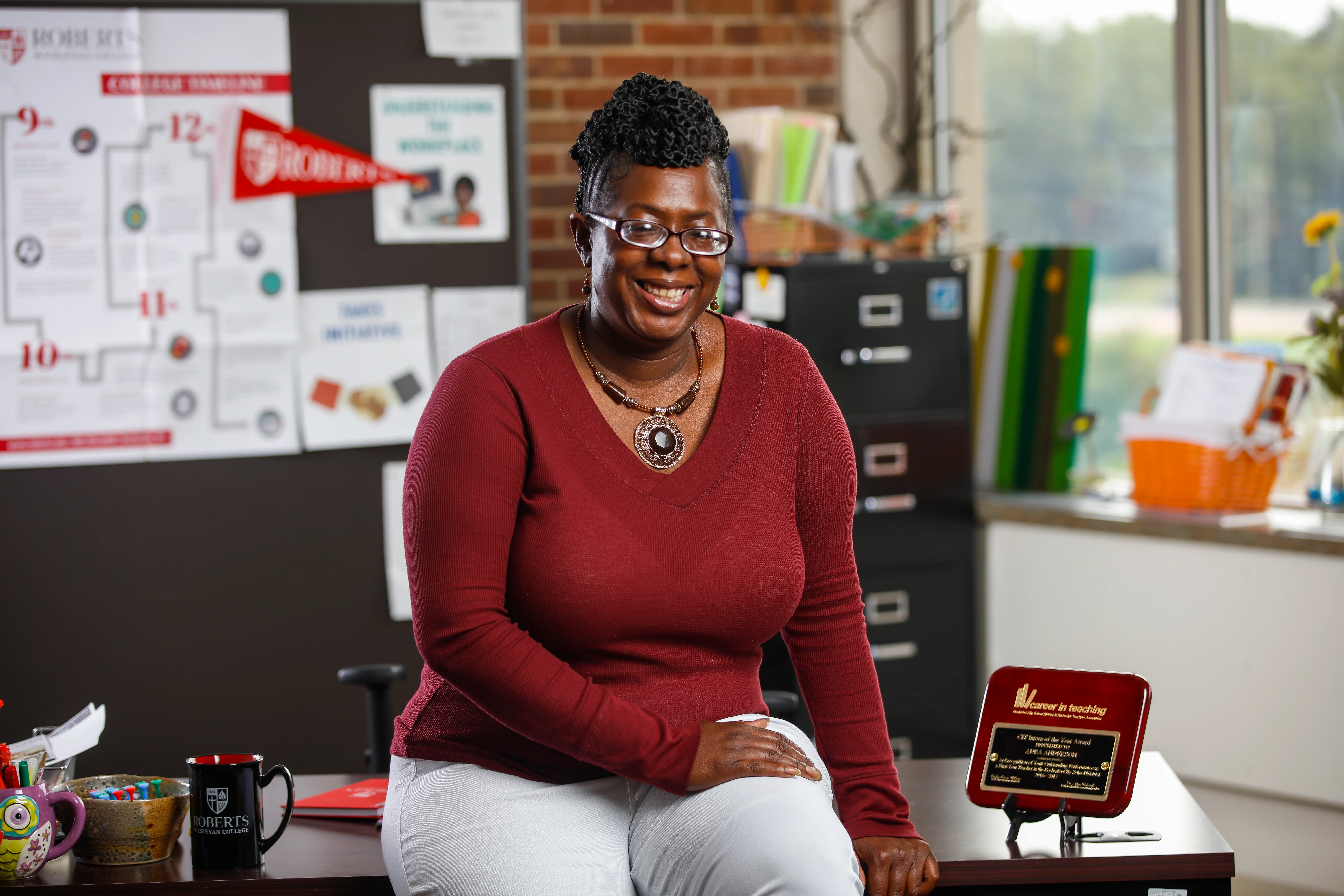 A teacher sits on a desk and smiles