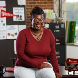 A teacher sits on a desk and smiles