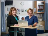 A nurse and nurse leader smile and stand together.