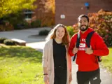 A young man and woman stand on campus and smile