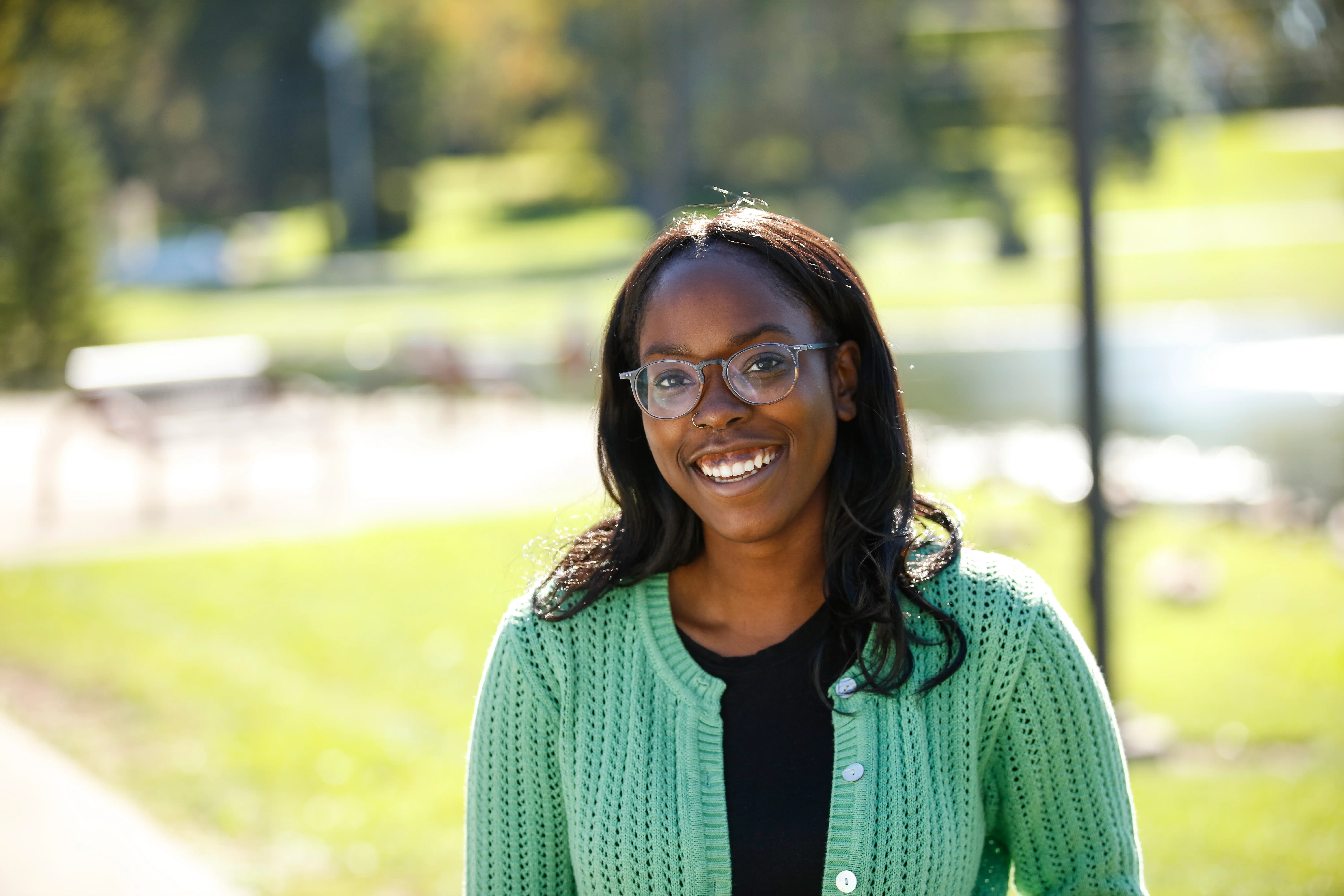 A young woman with glasses sits outside and smiles